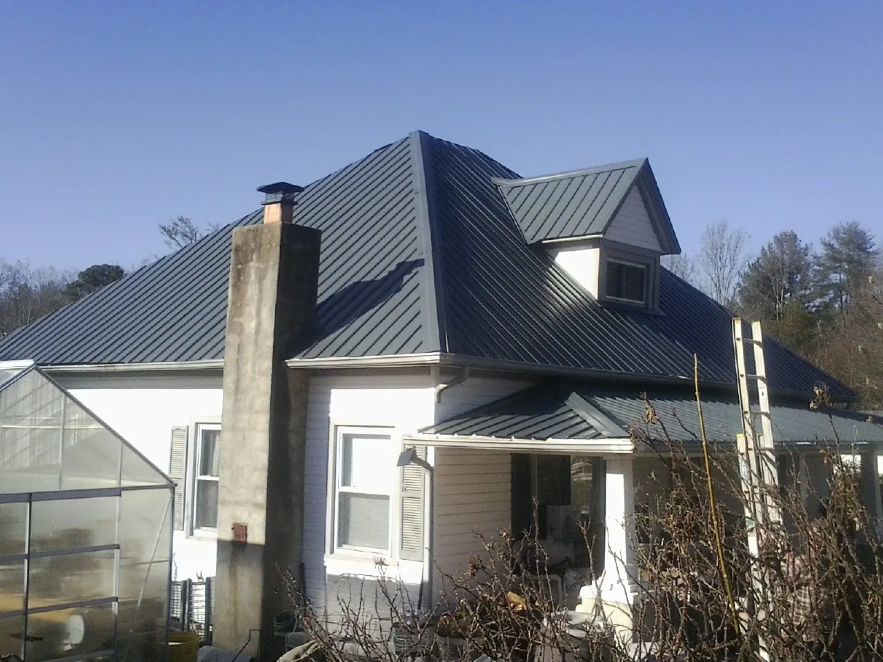 Dark blue standing seam metal roof on a white farmhouse with dormer — Slate & Tile Roof Repair by Roofing Brothers in Table Rock