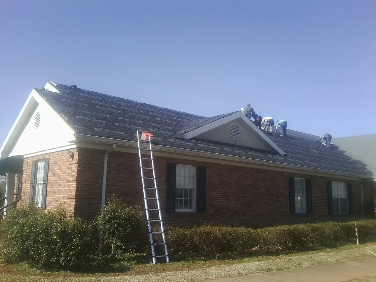 Crew tearing shingles off a brick ranch roof with a ladder set — Metal Roof Repair work by our crew in Table Rock