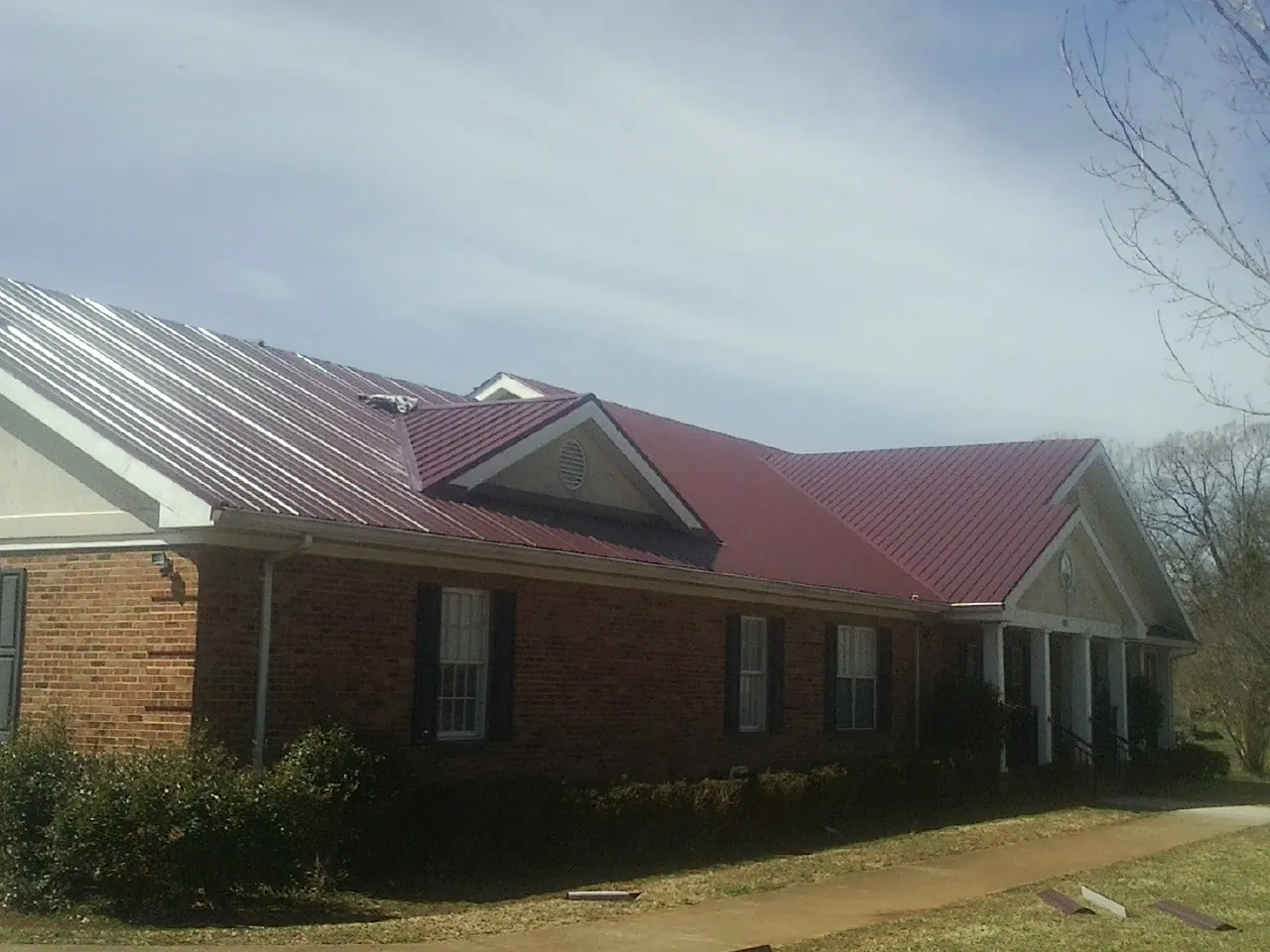 Red metal roof with gabled entries on a long brick building, from a Hail Damage Roof Repair job in Table Rock
