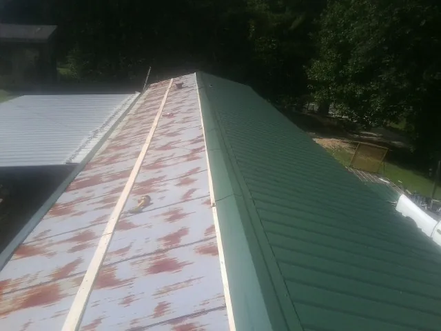 Old rusted panels beside newly installed green metal roofing — Wind Damage Roof Repair by Roofing Brothers in Table Rock