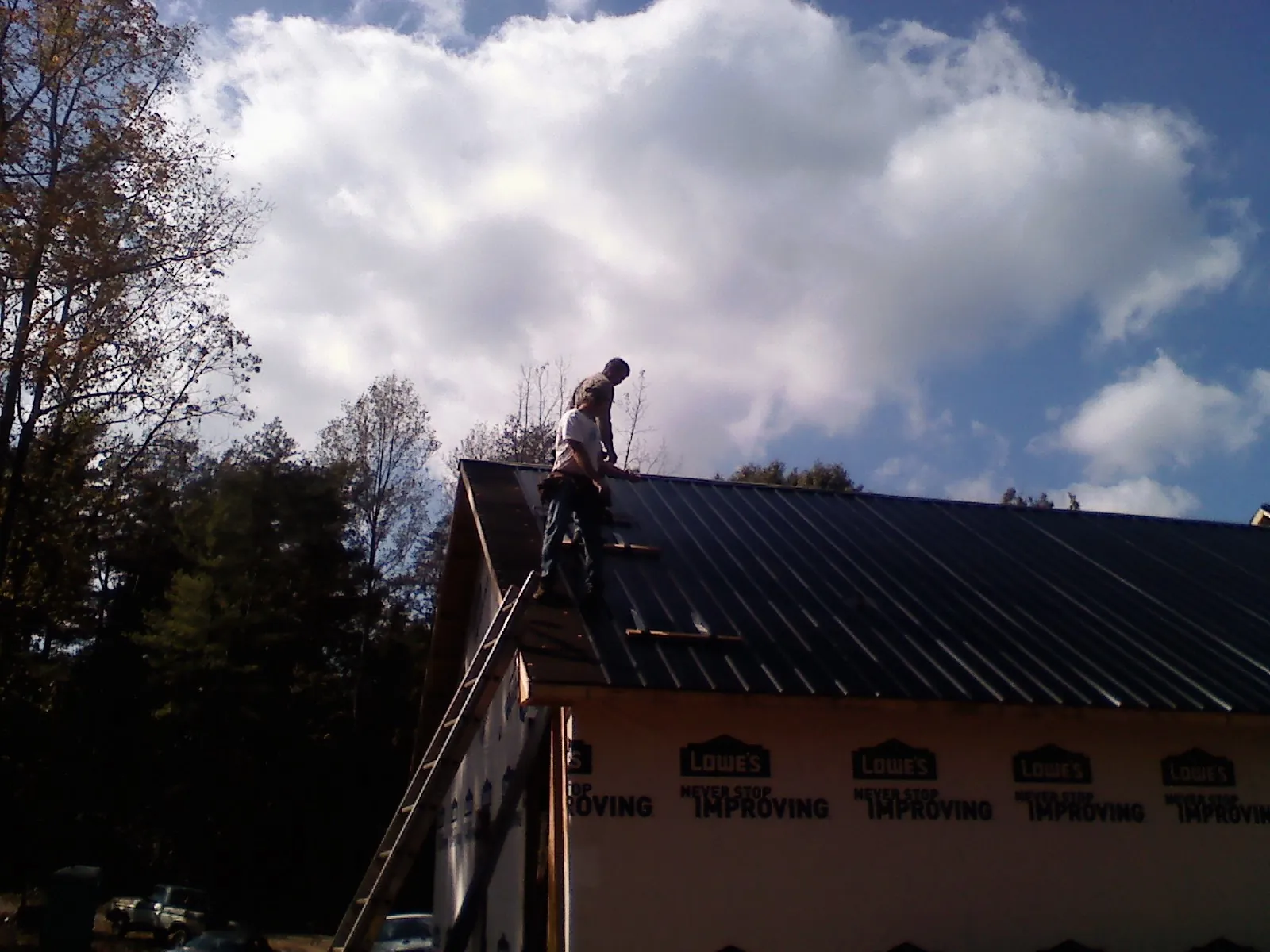 Roofer fastening dark metal panels high against a cloudy sky, from a Roof Inspection job in Table Rock